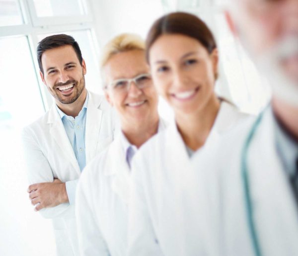 Closeup portrait of group of mixed age team of doctors in a line at a local hospital. There are two senior colleagues, and early 30's male and female colleagues. The man is in focus.